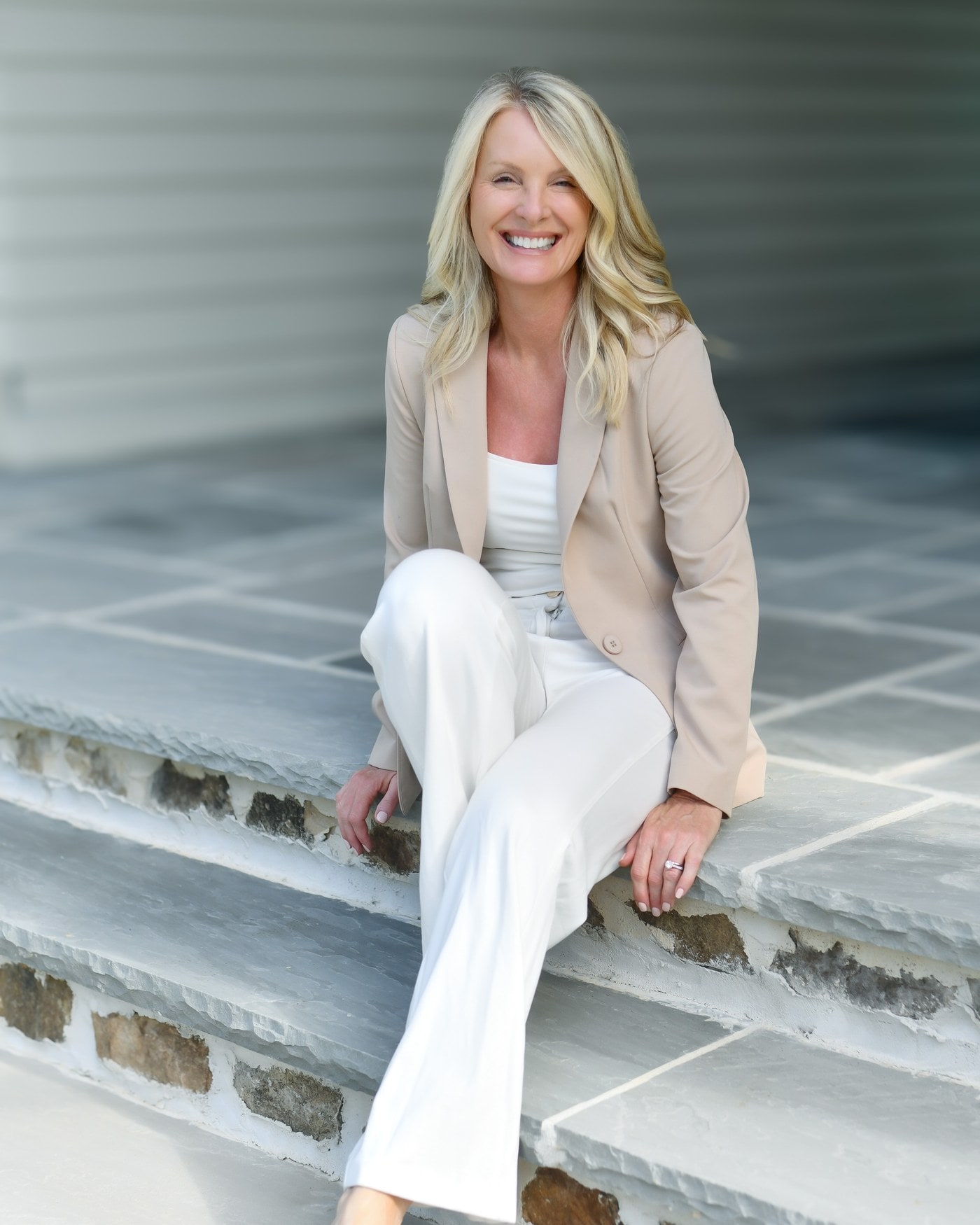 Kim Hedrick, REALTOR® with the Andy Bovender Team at Compass Carolinas, seated on stone steps in a tan blazer